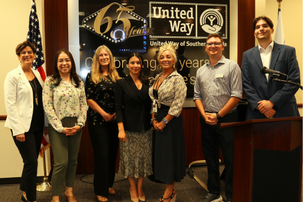 Tax assistance volunteers and UWSN staff standing in front of black, gold, and white UWSN logo in Boyd conference room