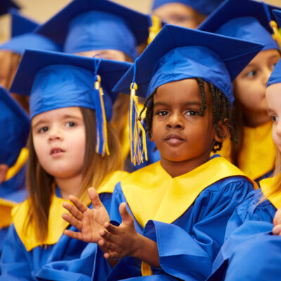 Toddler in a graduation gown clapping and smiling