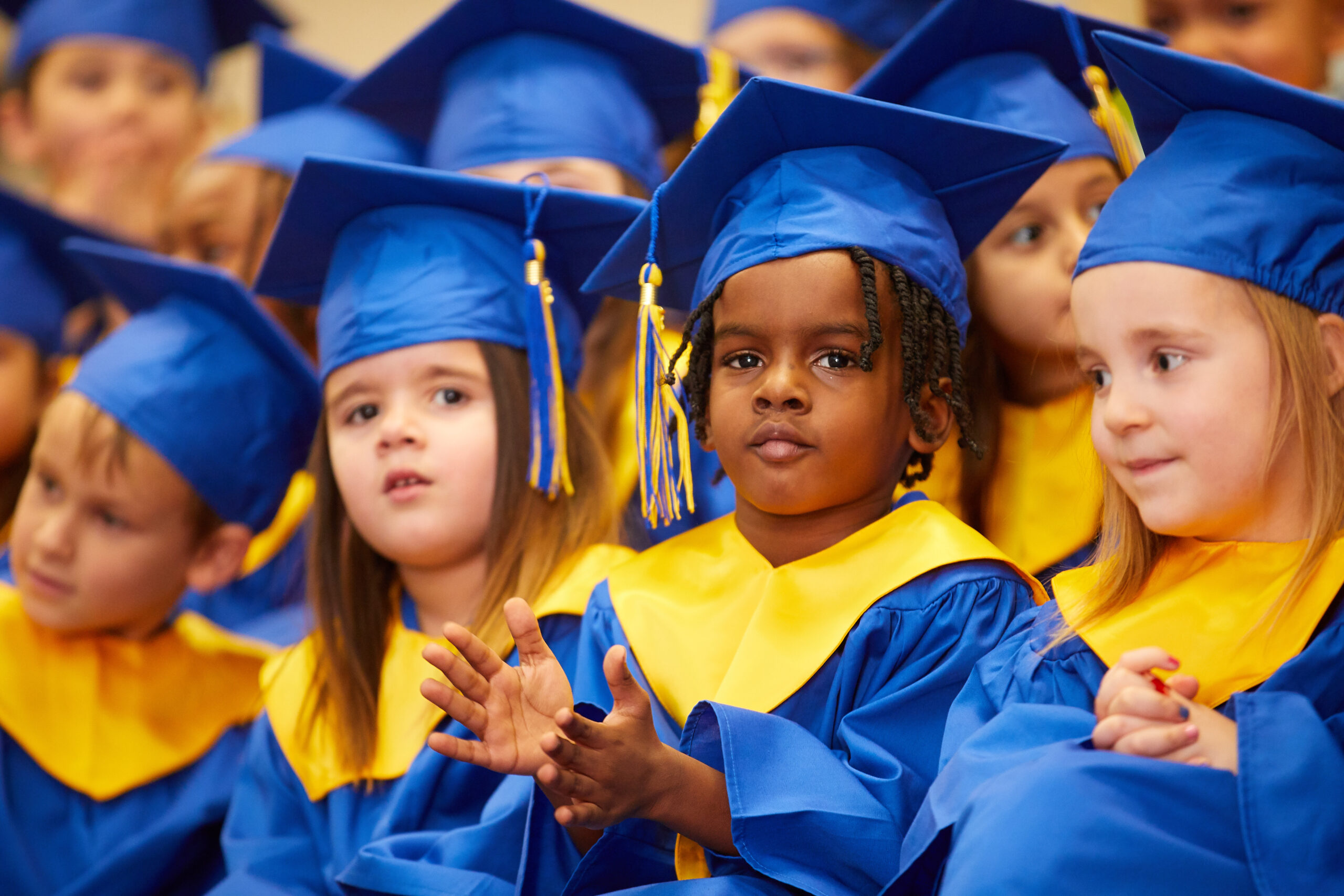 Toddler in a graduation gown clapping and smiling