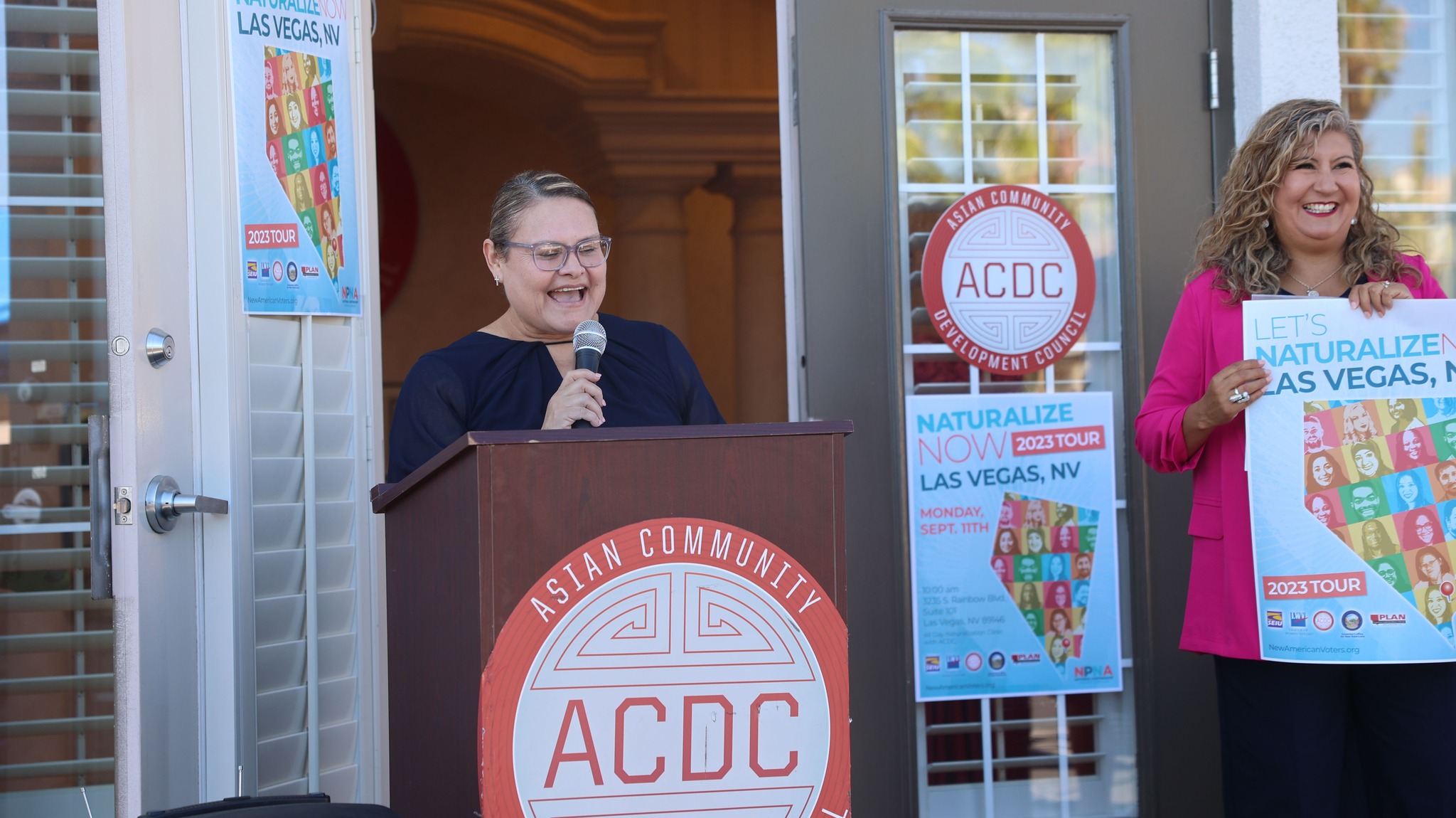 Palmira stands behind a podium with red and white ACDC Logo.