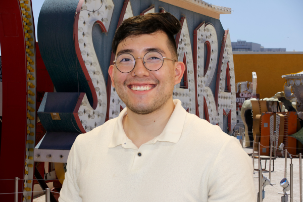 Henry Rosas in front of teal and red Sahara Las Vegas Sign. Henry is wearing a beige polo and wire frame glasses.