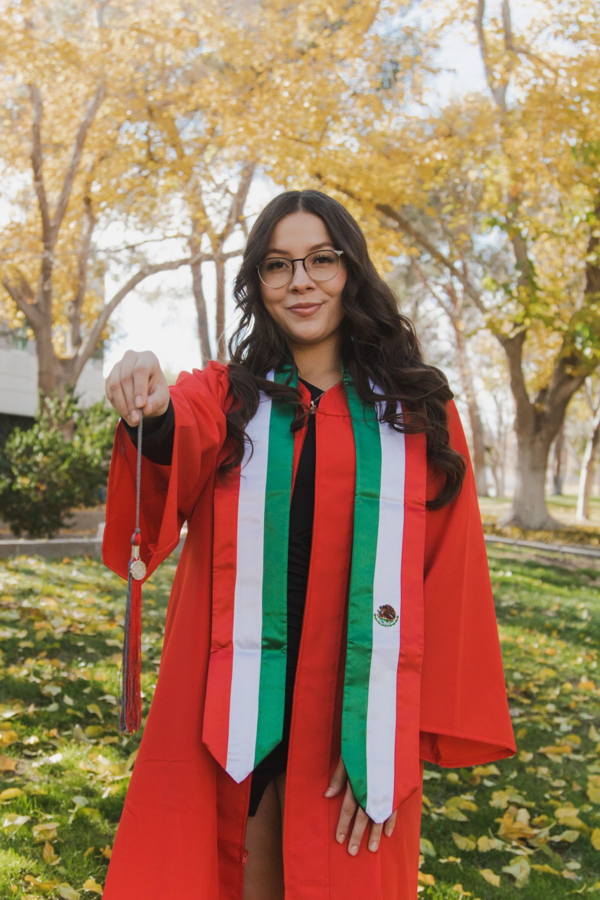 Alejandra has long dark brown hair and is in a red cap and gown with a red, white, and green sash.