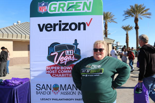 Dee in dark green sweatshirt standing in front of NFL Green sign.
