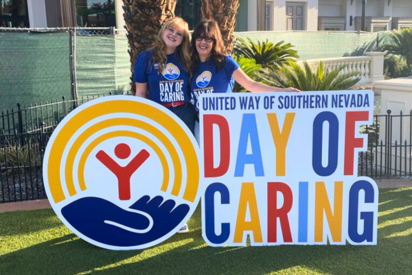 two women standing behind a brightly colored Day of Caring Sign