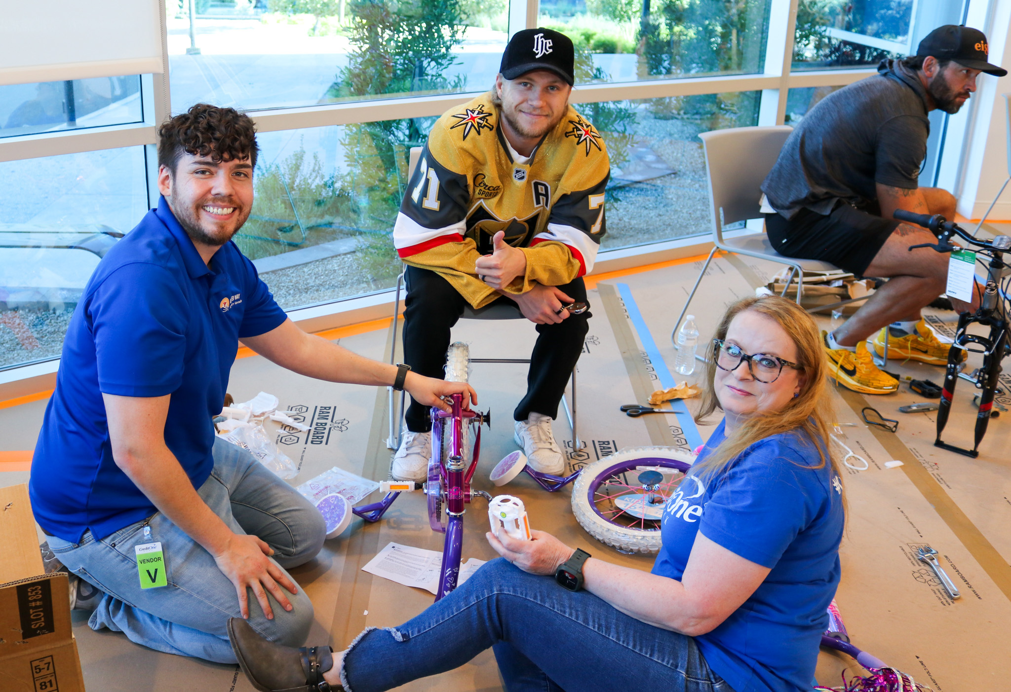 three people building a pink children's bicycle